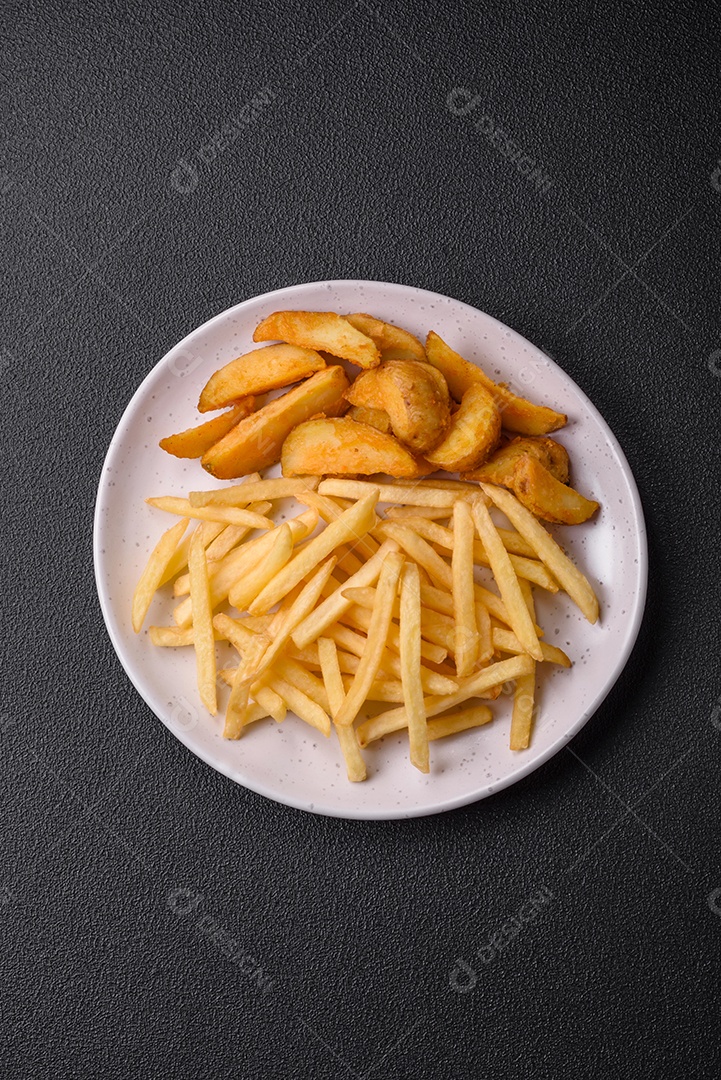 Deliciosas fatias de batata frita crocante com sal, especiarias e ervas sobre um fundo escuro de concreto