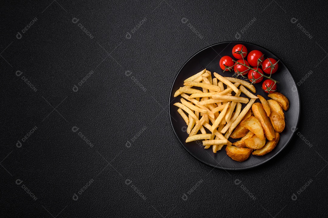 Deliciosas fatias de batata frita crocante com sal, especiarias e ervas sobre um fundo escuro de concreto