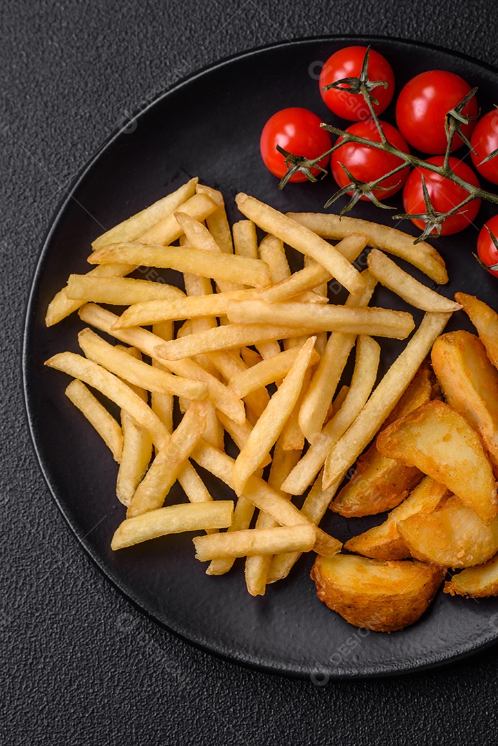 Deliciosas fatias de batata frita crocante com sal, especiarias e ervas sobre um fundo escuro de concreto