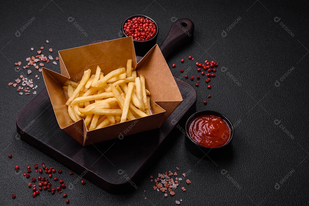 Deliciosas fatias de batata frita crocante com sal, especiarias e ervas sobre um fundo escuro de concreto