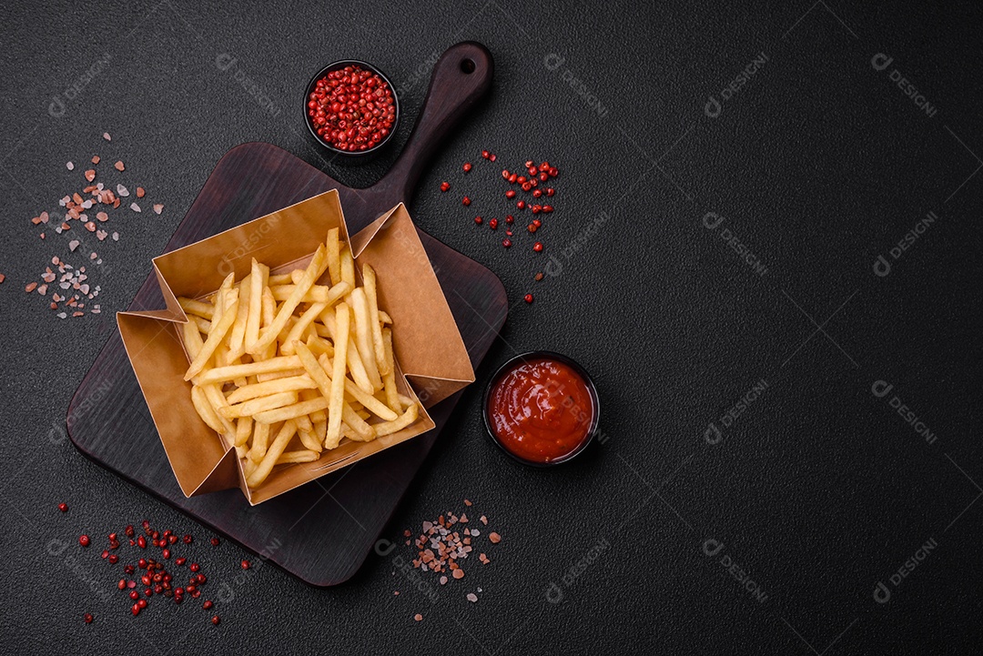 Deliciosas fatias de batata frita crocante com sal, especiarias e ervas sobre um fundo escuro de concreto