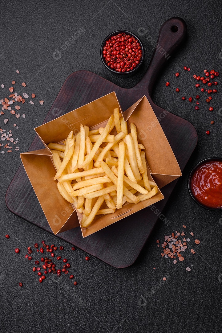 Deliciosas fatias de batata frita crocante com sal, especiarias e ervas sobre um fundo escuro de concreto