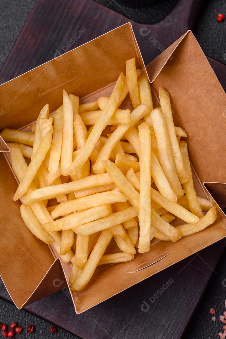 Deliciosas fatias de batata frita crocante com sal, especiarias e ervas sobre um fundo escuro de concreto