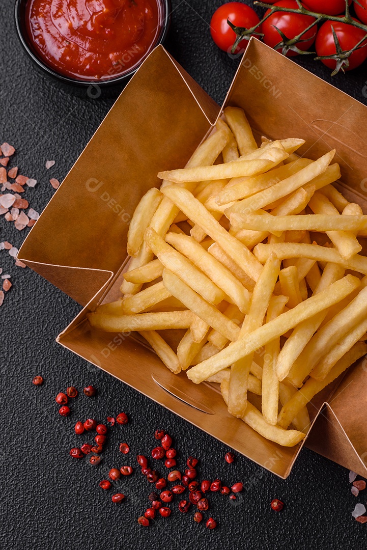 Deliciosas fatias de batata frita crocante com sal, especiarias e ervas sobre um fundo escuro de concreto
