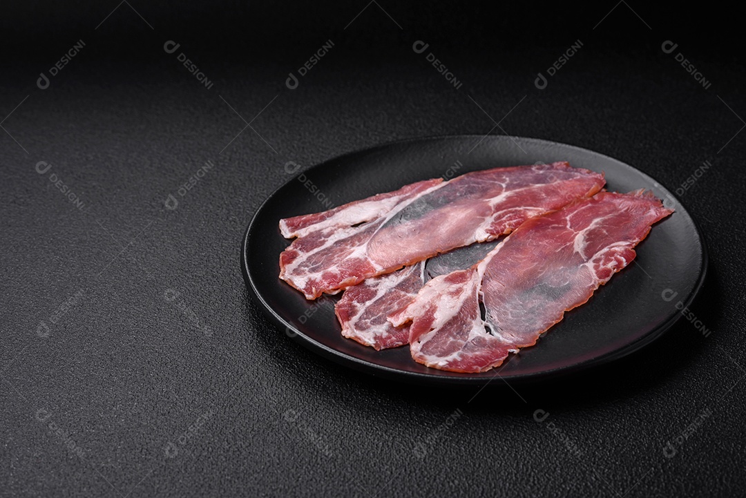 Fatias de delicioso jamon ou presunto defumado com sal, especiarias e ervas sobre um fundo escuro de concreto