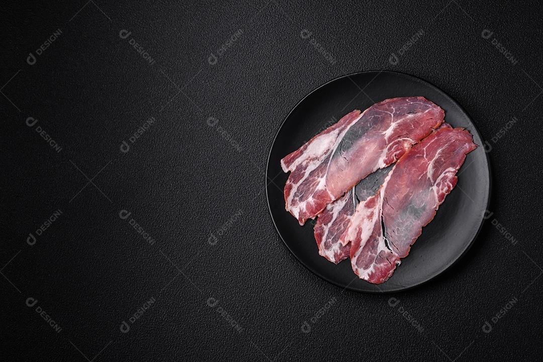 Fatias de delicioso jamon ou presunto defumado com sal, especiarias e ervas sobre um fundo escuro de concreto