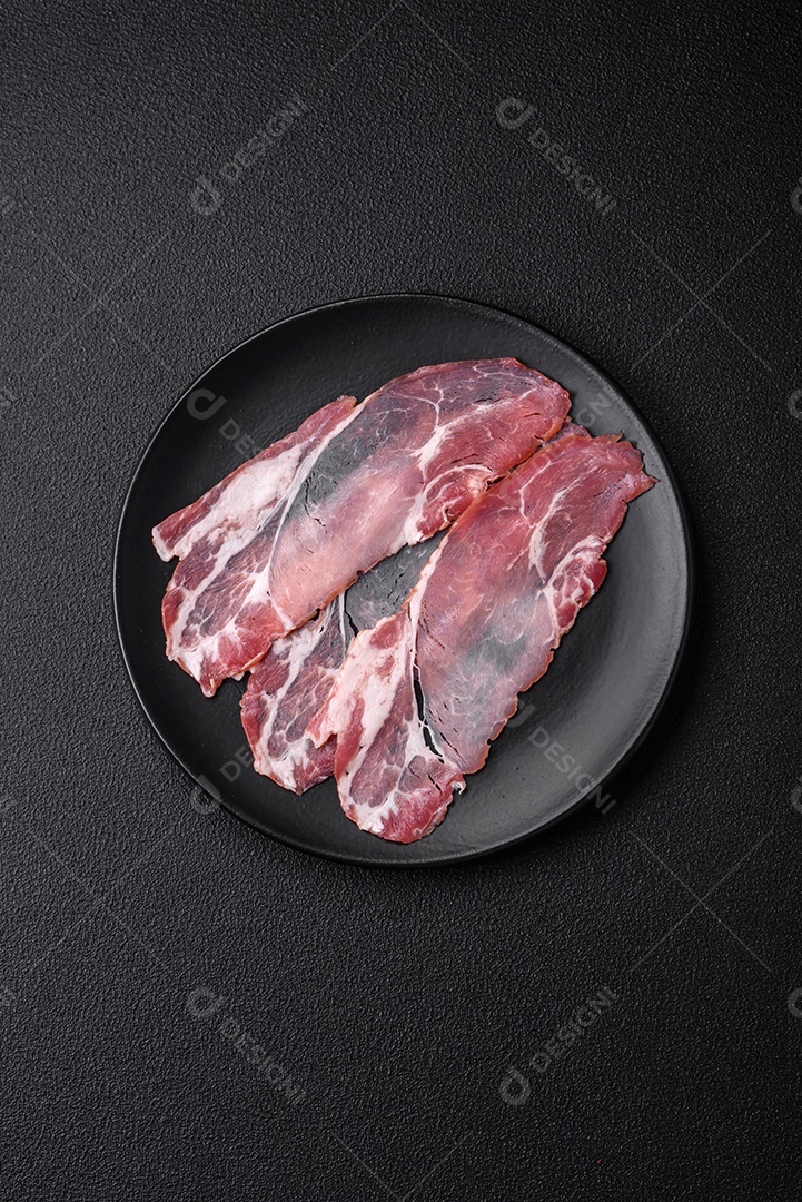 Fatias de delicioso jamon ou presunto defumado com sal, especiarias e ervas sobre um fundo escuro de concreto