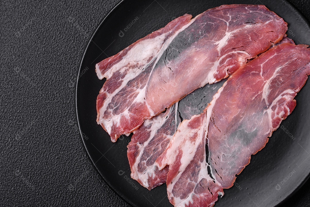 Fatias de delicioso jamon ou presunto defumado com sal, especiarias e ervas sobre um fundo escuro de concreto