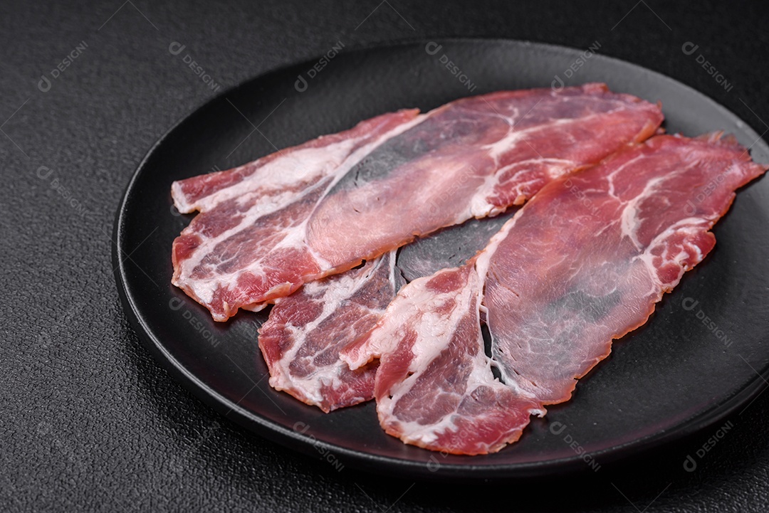 Fatias de delicioso jamon ou presunto defumado com sal, especiarias e ervas sobre um fundo escuro de concreto