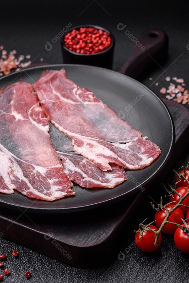 Fatias de delicioso jamon ou presunto defumado com sal, especiarias e ervas sobre um fundo escuro de concreto