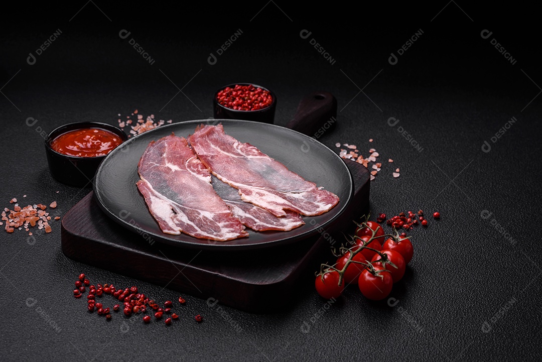 Fatias de delicioso jamon ou presunto defumado com sal, especiarias e ervas sobre um fundo escuro de concreto