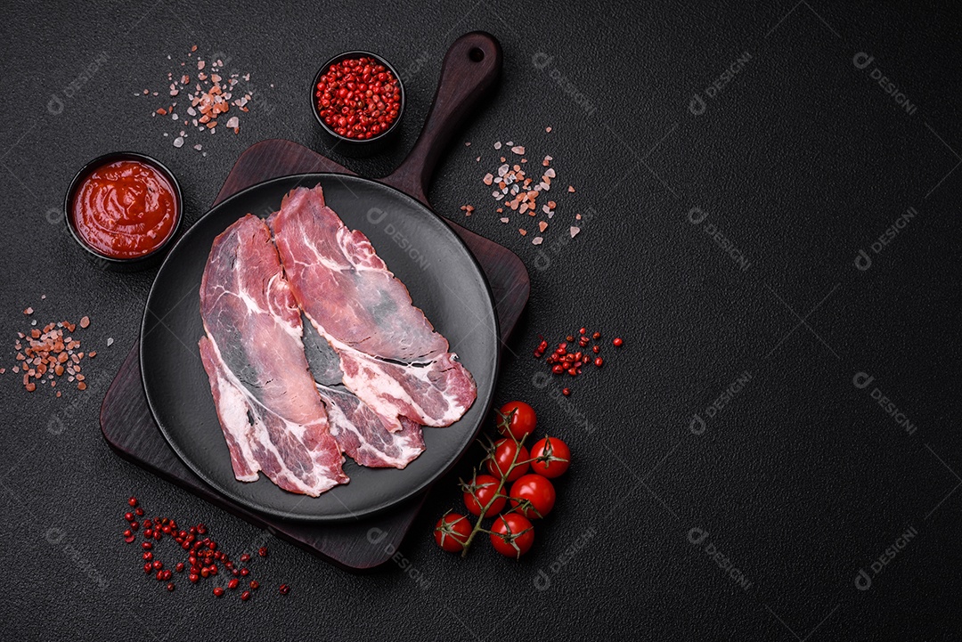 Fatias de delicioso jamon ou presunto defumado com sal, especiarias e ervas sobre um fundo escuro de concreto
