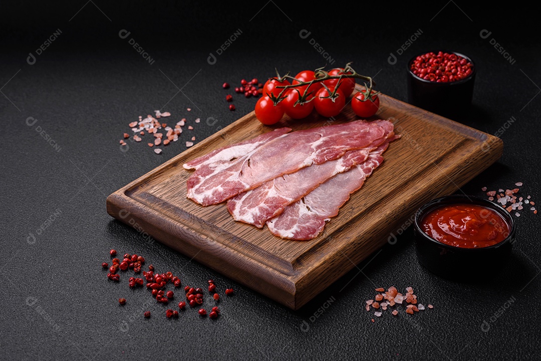 Fatias de delicioso jamon ou presunto defumado com sal, especiarias e ervas sobre um fundo escuro de concreto