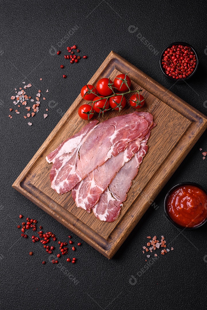 Fatias de delicioso jamon ou presunto defumado com sal, especiarias e ervas sobre um fundo escuro de concreto