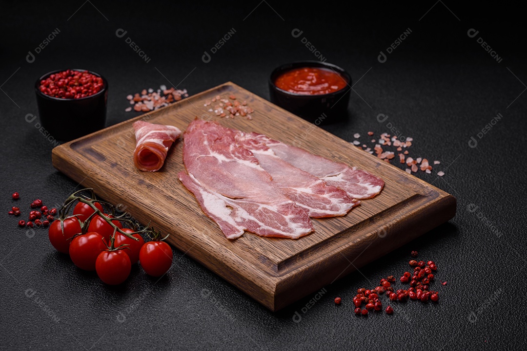 Fatias de delicioso jamon ou presunto defumado com sal, especiarias e ervas sobre um fundo escuro de concreto