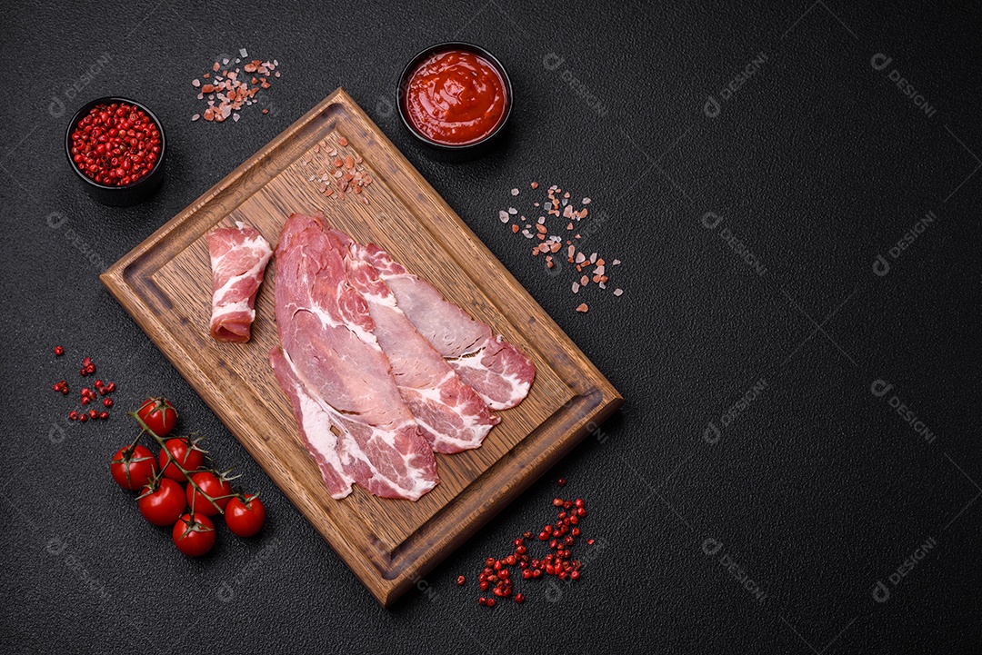 Fatias de delicioso jamon ou presunto defumado com sal, especiarias e ervas sobre um fundo escuro de concreto