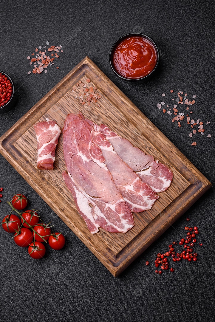 Fatias de delicioso jamon ou presunto defumado com sal, especiarias e ervas sobre um fundo escuro de concreto