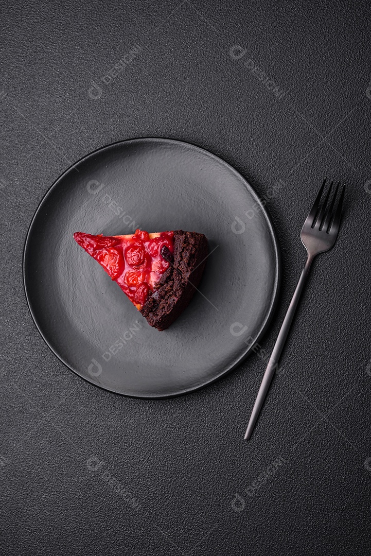 Linda e saborosa fatia doce de cheesecake com cereja em uma placa de cerâmica sobre um fundo escuro de concreto