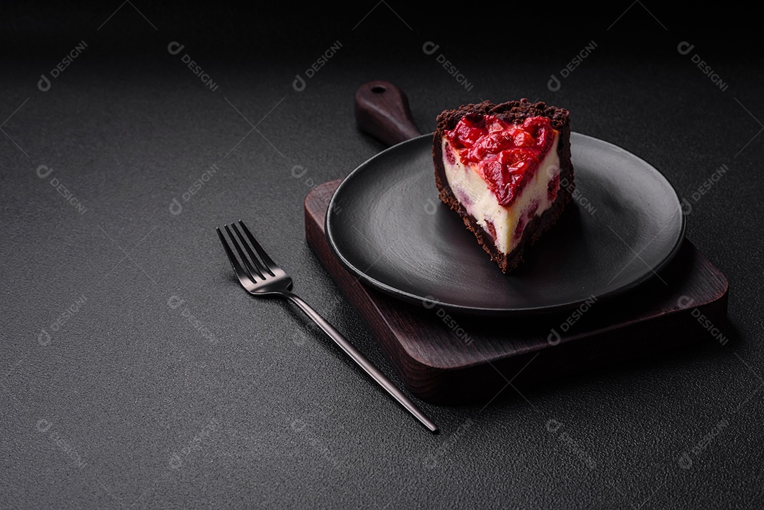 Linda e saborosa fatia doce de cheesecake com cereja em uma placa de cerâmica sobre um fundo escuro de concreto