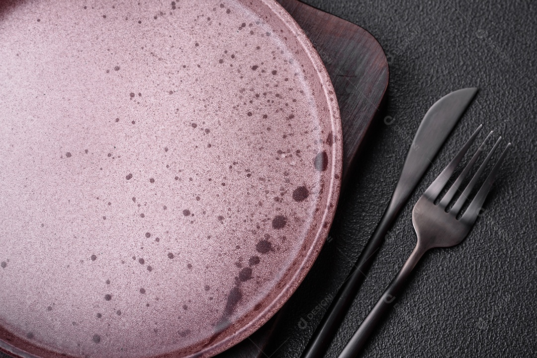 Prato cerâmico vazio em um fundo escuro texturizado. Preparando utensílios de cozinha para um jantar em família
