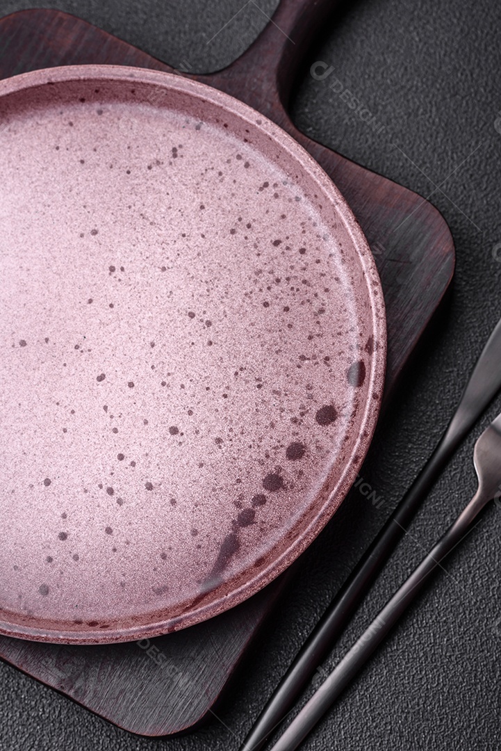 Prato cerâmico vazio em um fundo escuro texturizado. Preparando utensílios de cozinha para um jantar em família