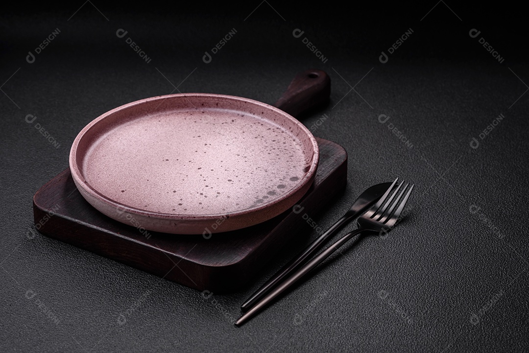 Prato cerâmico vazio em um fundo escuro texturizado. Preparando utensílios de cozinha para um jantar em família