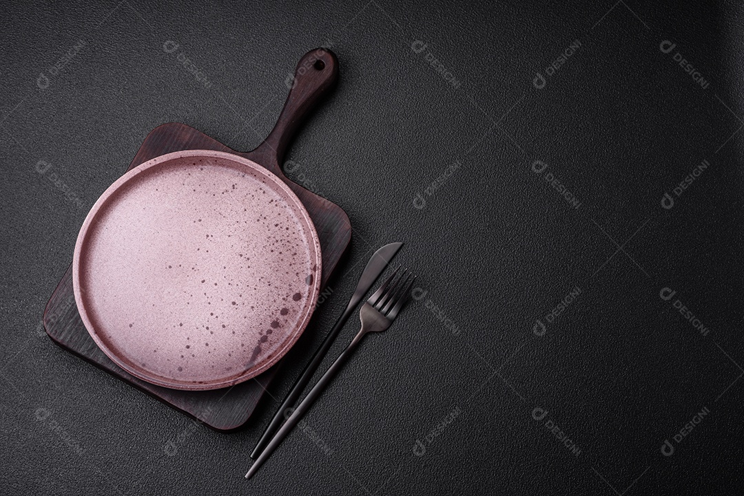 Prato cerâmico vazio em um fundo escuro texturizado. Preparando utensílios de cozinha para um jantar em família