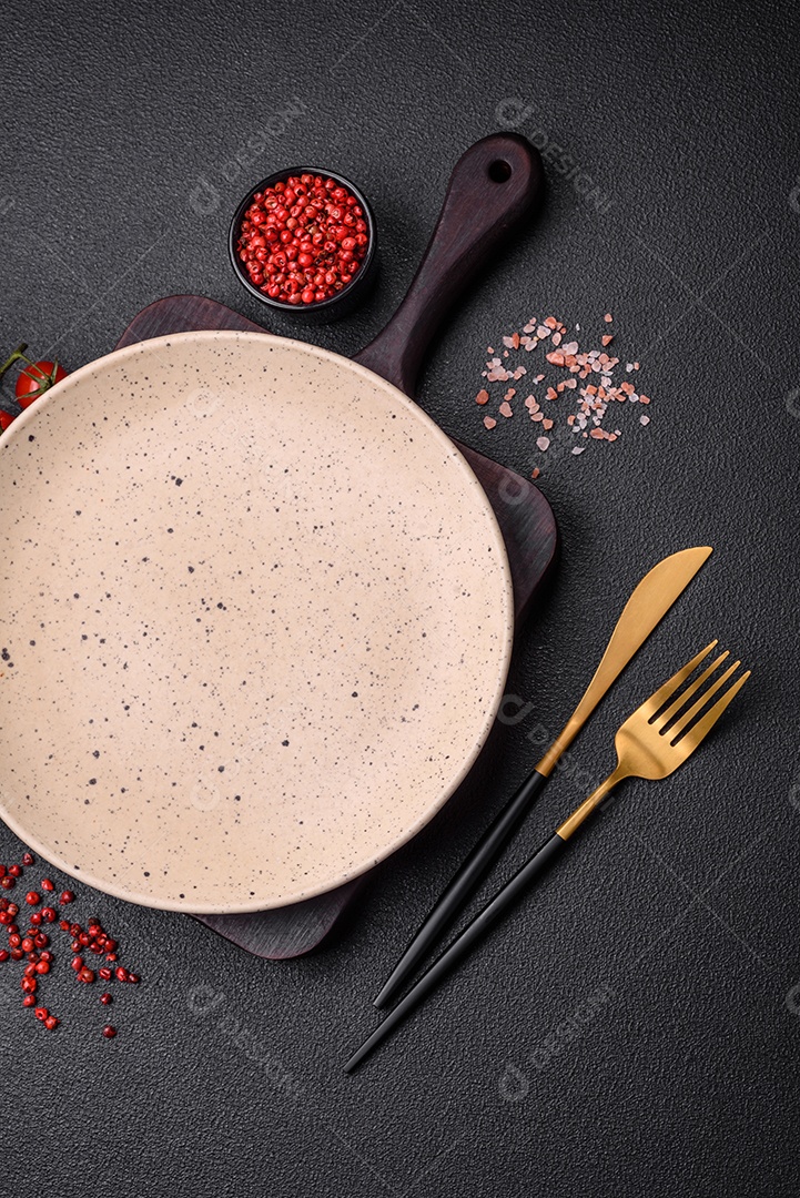 Prato cerâmico vazio em um fundo escuro texturizado. Preparando utensílios de cozinha para um jantar em família