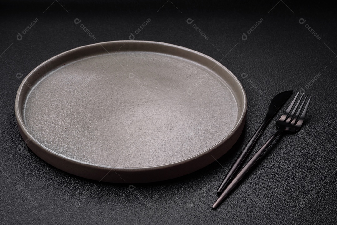 Prato cerâmico vazio em um fundo escuro texturizado. Preparando utensílios de cozinha para um jantar em família