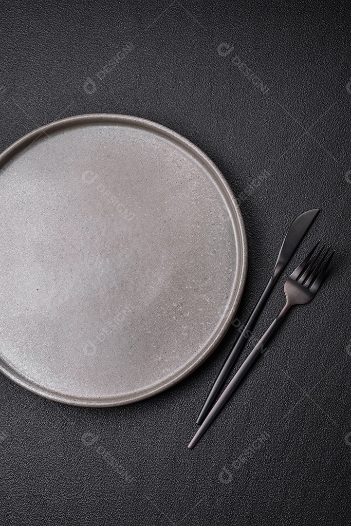 Prato cerâmico vazio em um fundo escuro texturizado. Preparando utensílios de cozinha para um jantar em família