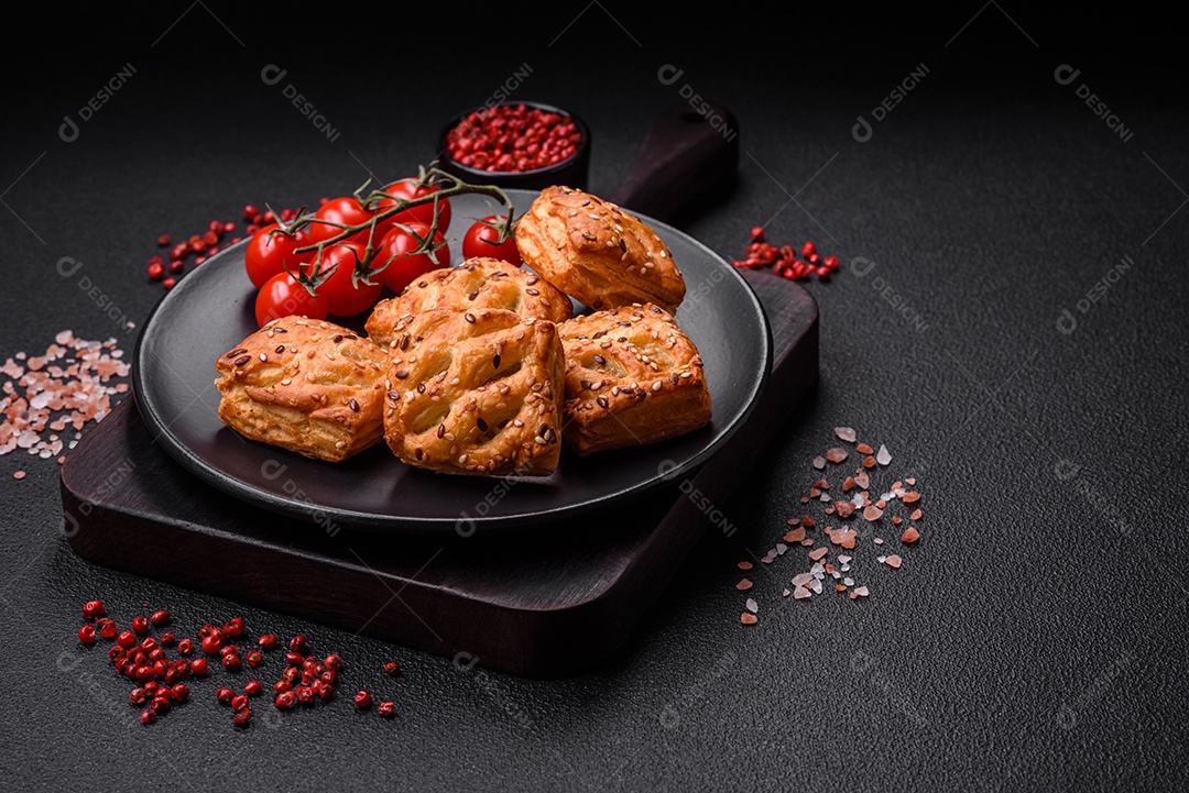 Deliciosos mini folhados crocantes com salsicha ou carne com sal, tomilho e gergelim sobre fundo escuro de concreto