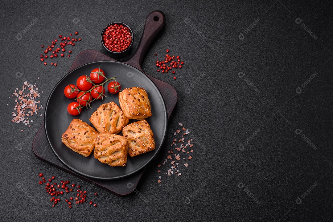Deliciosos mini folhados crocantes com salsicha ou carne com sal, tomilho e gergelim sobre fundo escuro de concreto
