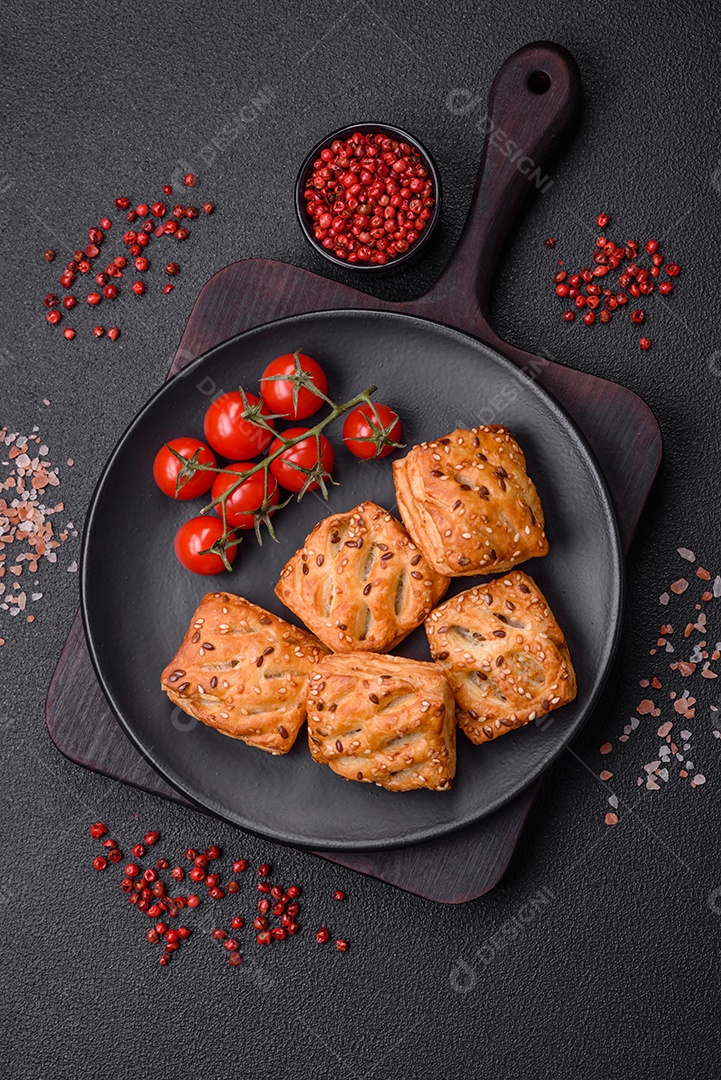 Deliciosos mini folhados crocantes com salsicha ou carne com sal, tomilho e gergelim sobre fundo escuro de concreto