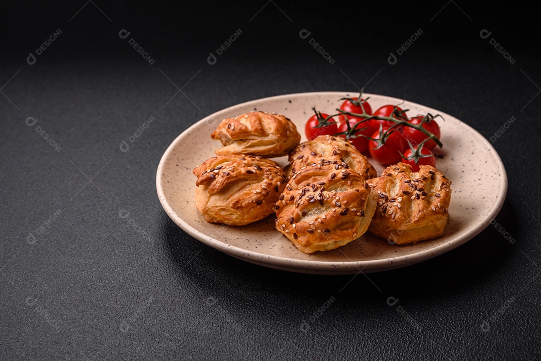 Deliciosos mini folhados crocantes com salsicha ou carne com sal, tomilho e gergelim sobre fundo escuro de concreto