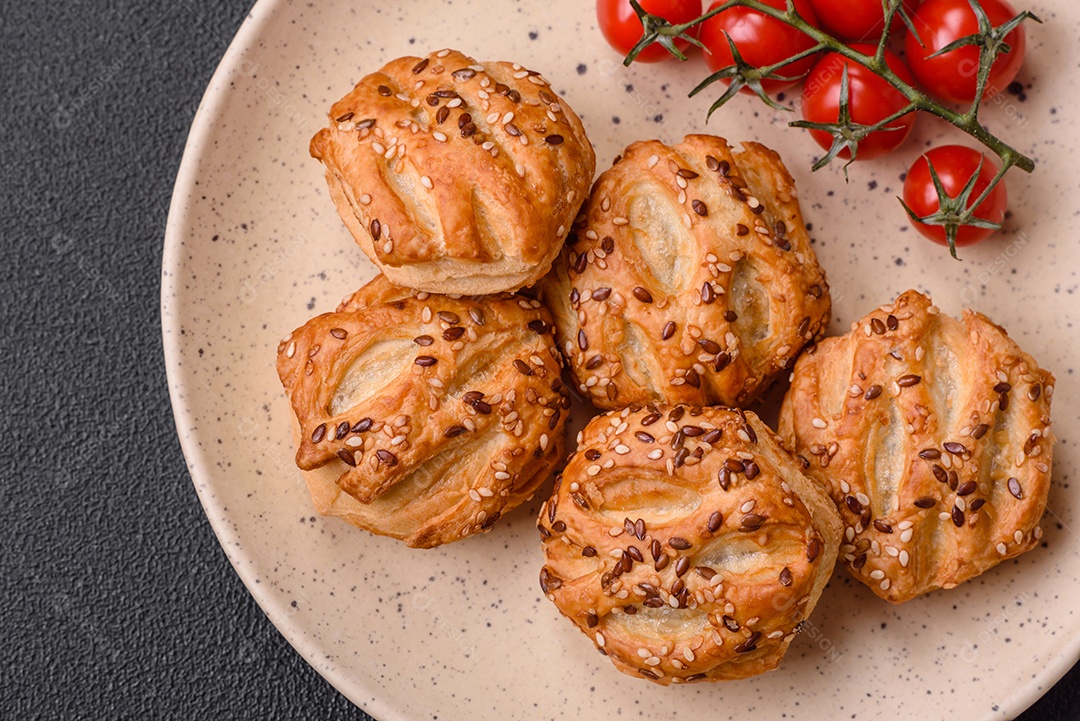 Deliciosos mini folhados crocantes com salsicha ou carne com sal, tomilho e gergelim sobre fundo escuro de concreto