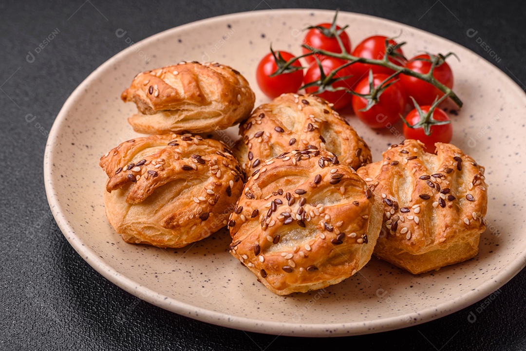 Deliciosos mini folhados crocantes com salsicha ou carne com sal, tomilho e gergelim sobre fundo escuro de concreto