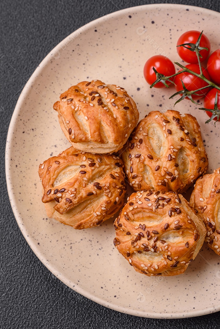 Deliciosos mini folhados crocantes com salsicha ou carne com sal, tomilho e gergelim sobre fundo escuro de concreto