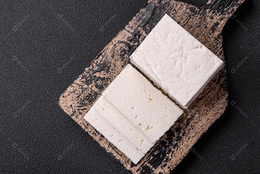 Delicioso queijo ricota fresco cortado em fatias com legumes, sal e especiarias sobre um fundo escuro de concreto