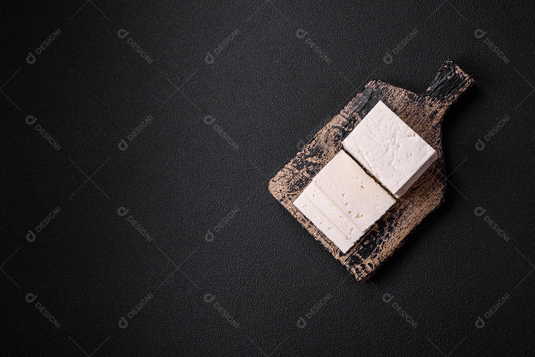 Delicioso queijo ricota fresco cortado em fatias com legumes, sal e especiarias sobre um fundo escuro de concreto