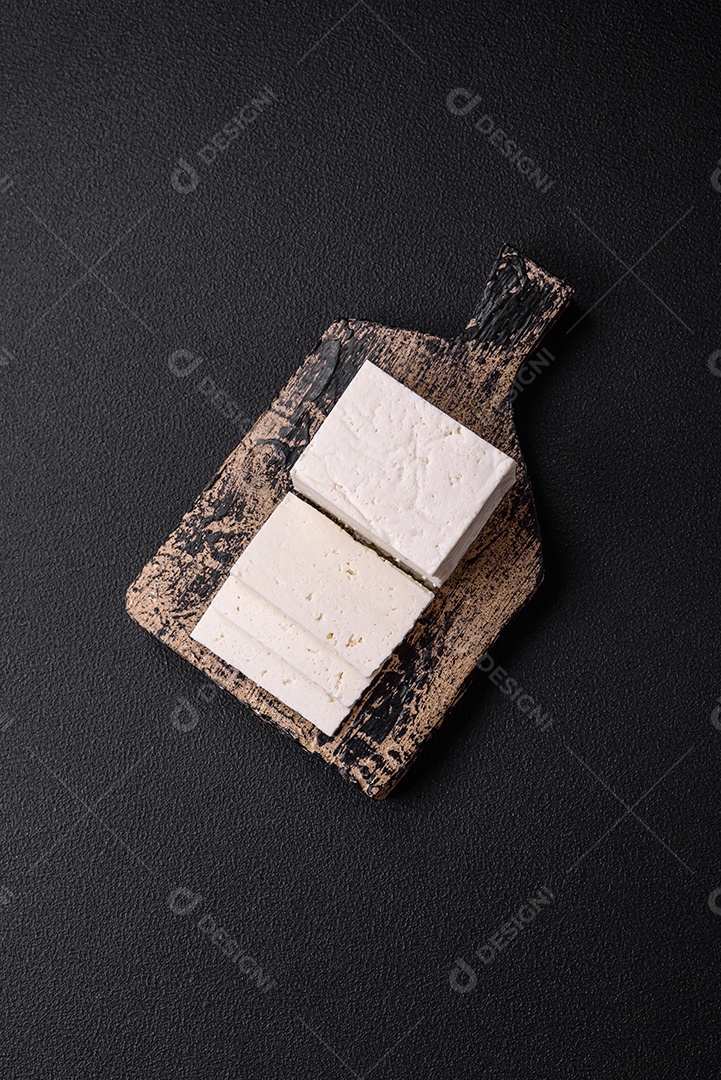 Delicioso queijo ricota fresco cortado em fatias com legumes, sal e especiarias sobre um fundo escuro de concreto