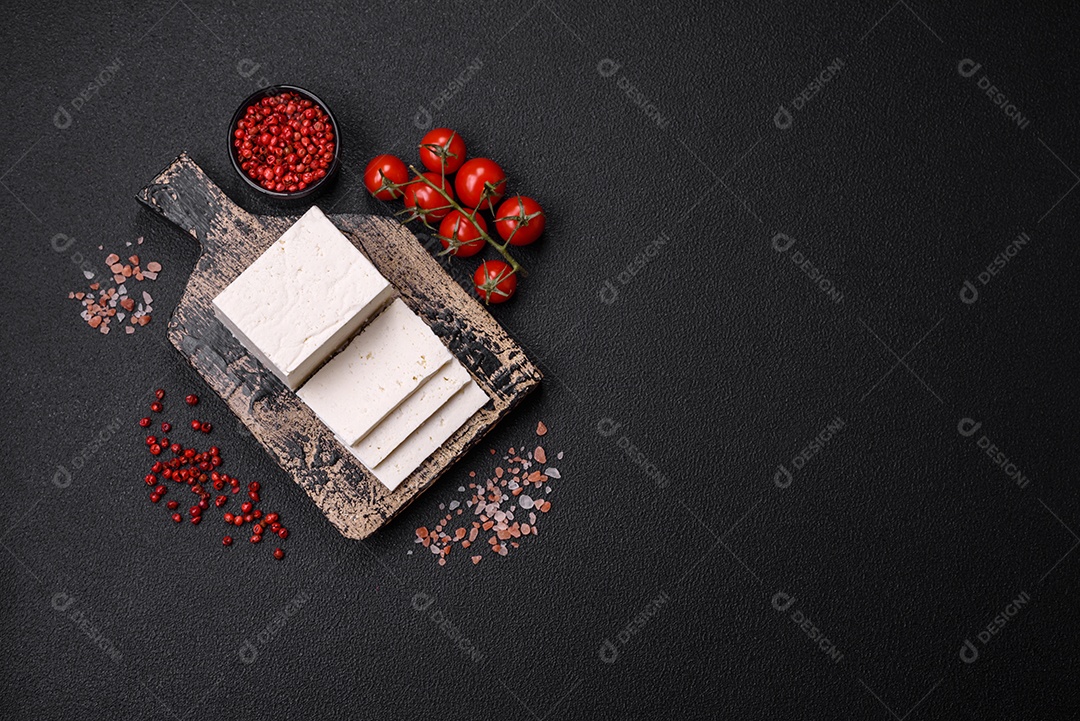 Delicioso queijo ricota fresco cortado em fatias com legumes, sal e especiarias sobre um fundo escuro de concreto