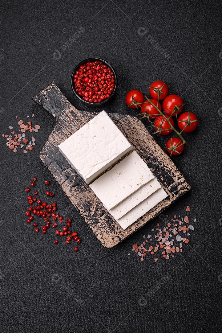 Delicioso queijo ricota fresco cortado em fatias com legumes, sal e especiarias sobre um fundo escuro de concreto