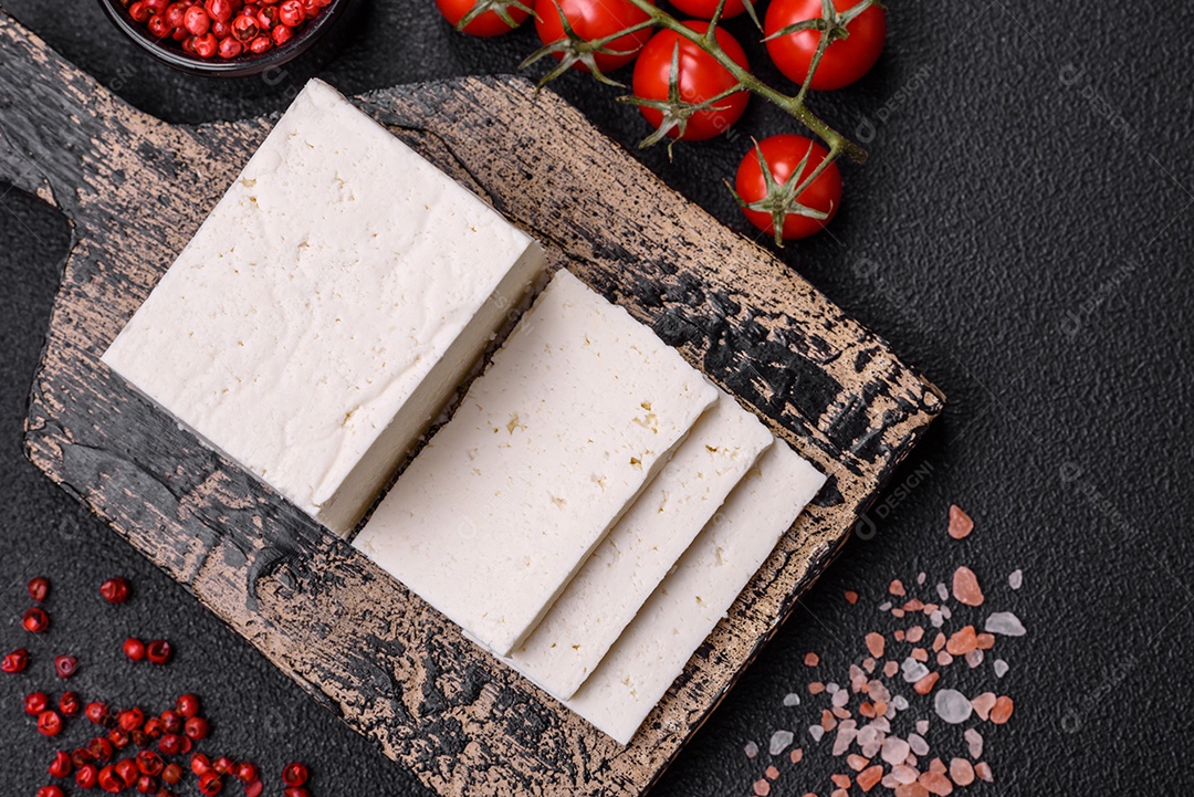 Delicioso queijo ricota fresco cortado em fatias com legumes, sal e especiarias sobre um fundo escuro de concreto