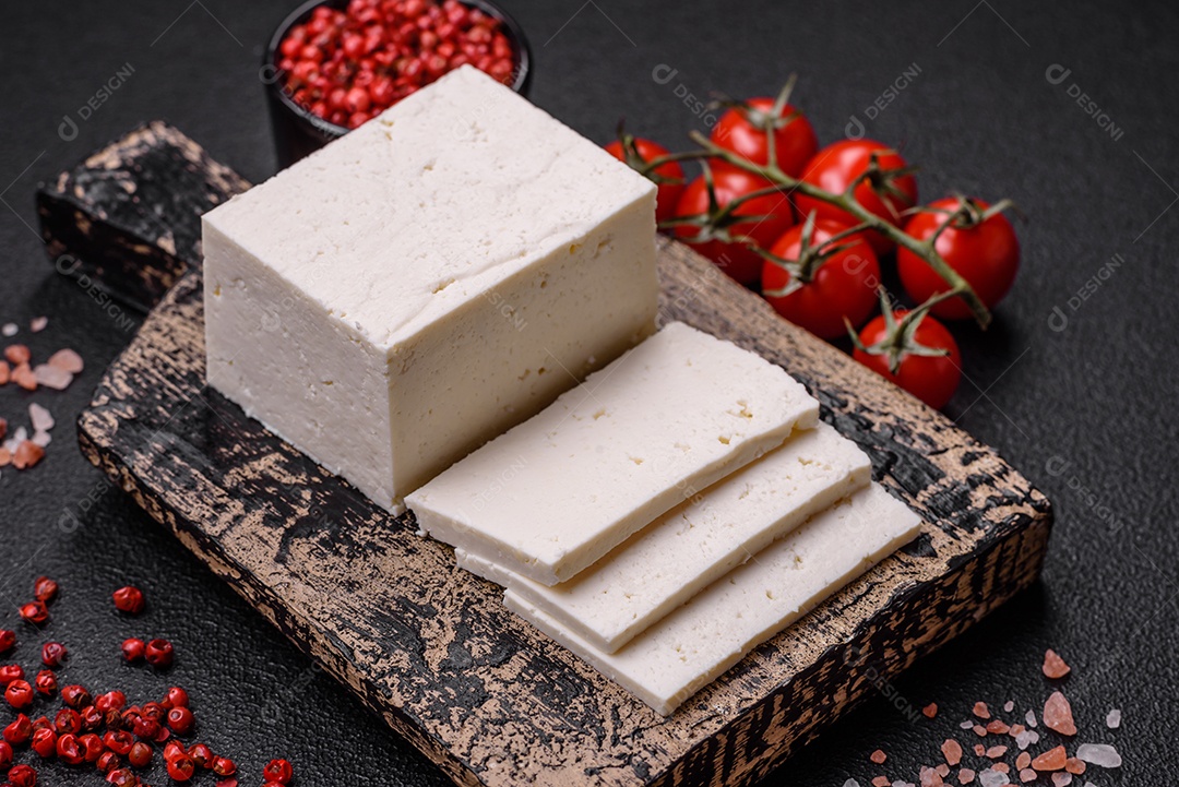 Delicioso queijo ricota fresco cortado em fatias com legumes, sal e especiarias sobre um fundo escuro de concreto
