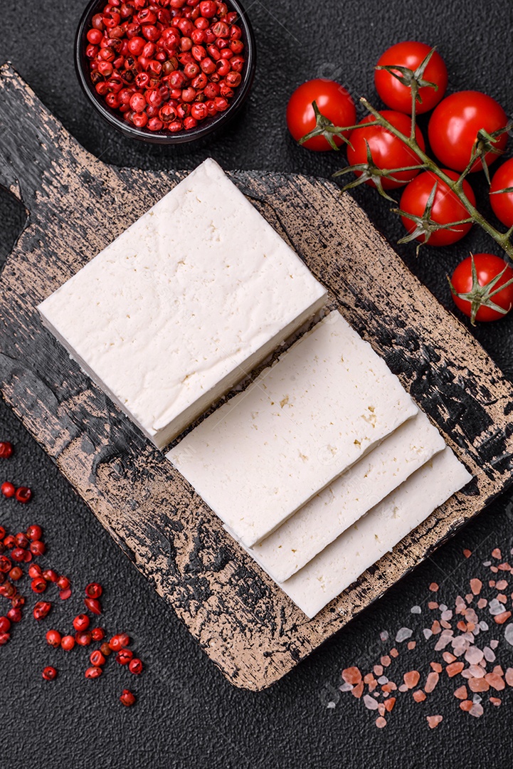 Delicioso queijo ricota fresco cortado em fatias com legumes, sal e especiarias sobre um fundo escuro de concreto