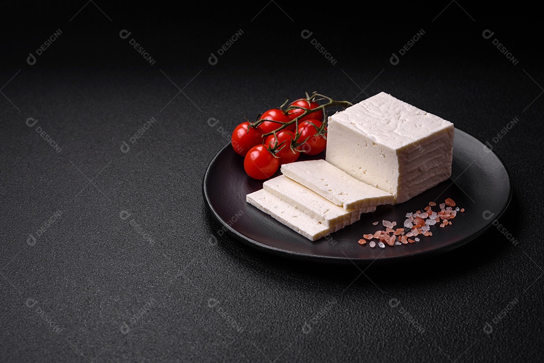 Delicioso queijo ricota fresco cortado em fatias com legumes, sal e especiarias sobre um fundo escuro de concreto