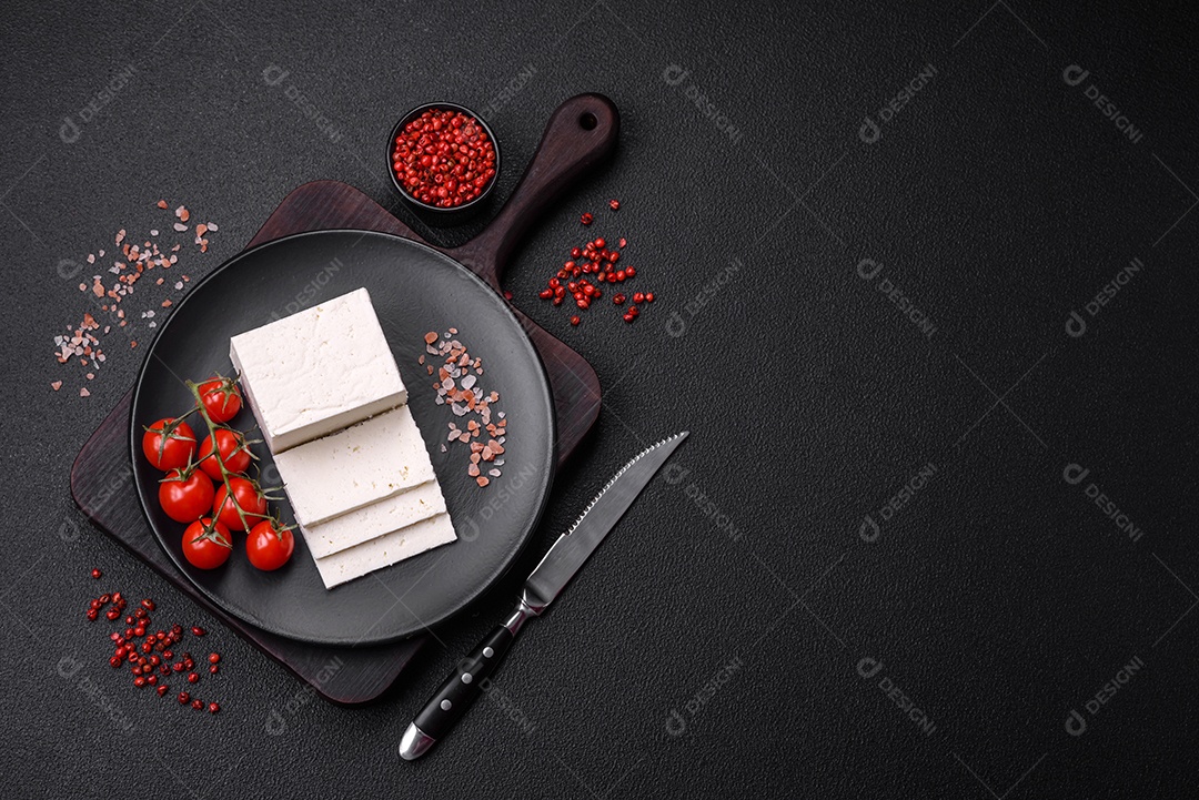 Delicioso queijo ricota fresco cortado em fatias com legumes, sal e especiarias sobre um fundo escuro de concreto
