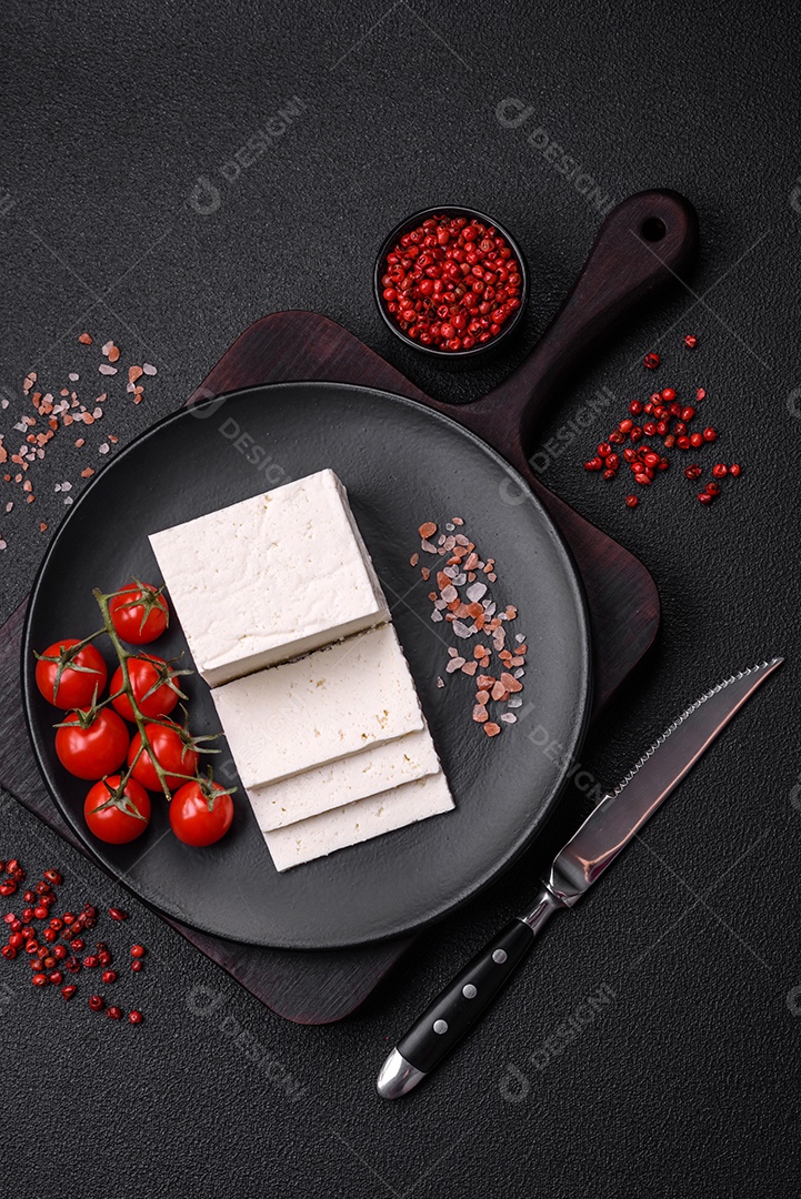Delicioso queijo ricota fresco cortado em fatias com legumes, sal e especiarias sobre um fundo escuro de concreto
