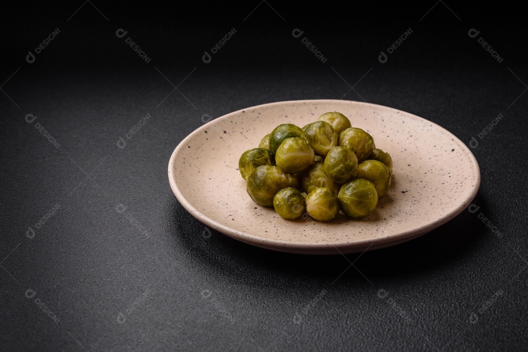 Deliciosas couves de Bruxelas cozidas em um prato de cerâmica sobre um fundo escuro de concreto. Comida vegetariana