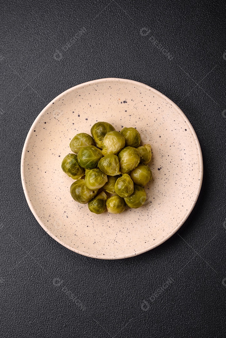 Deliciosas couves de Bruxelas cozidas em um prato de cerâmica sobre um fundo escuro de concreto. Comida vegetariana
